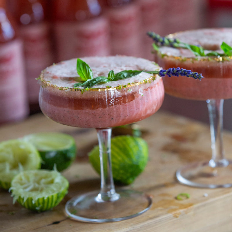Two pink basil smash strawberry colada cocktails in gold-rimmed glasses with lime
