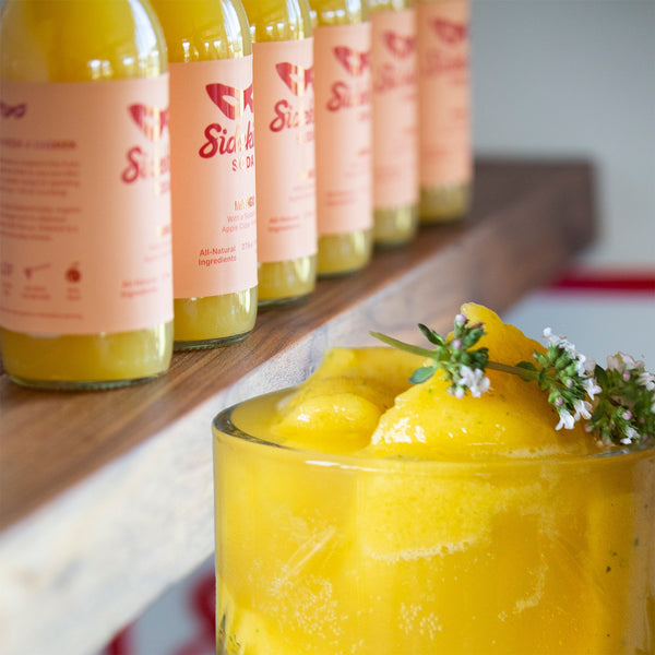 Glass of yellow mango peach slushy with Sidekick Mango bottles behind