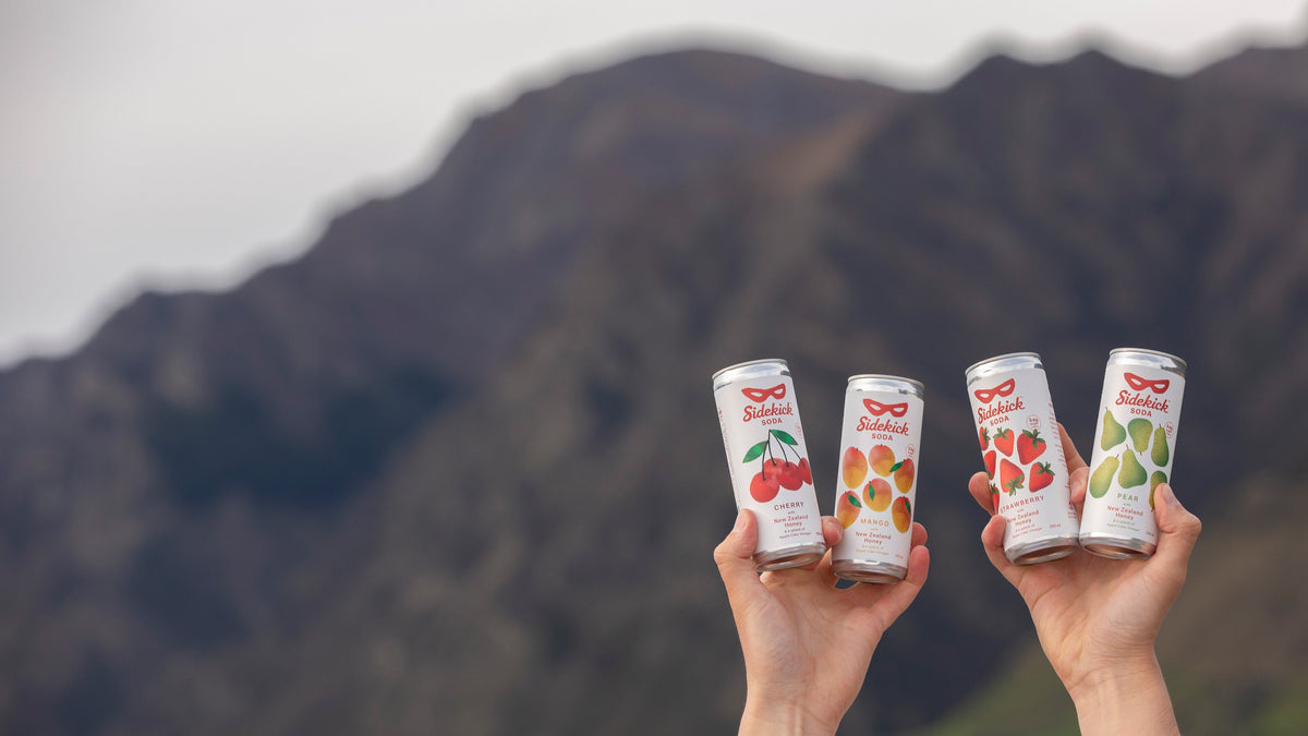 Four Sidekick Soda cans against a New Zealand mountain backdrop